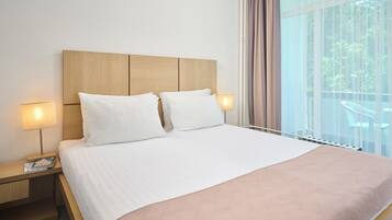 Habitación de hotel con una cama grande, dos lámparas de noche, una mesita de noche y vistas al exterior a través de amplias ventanas.