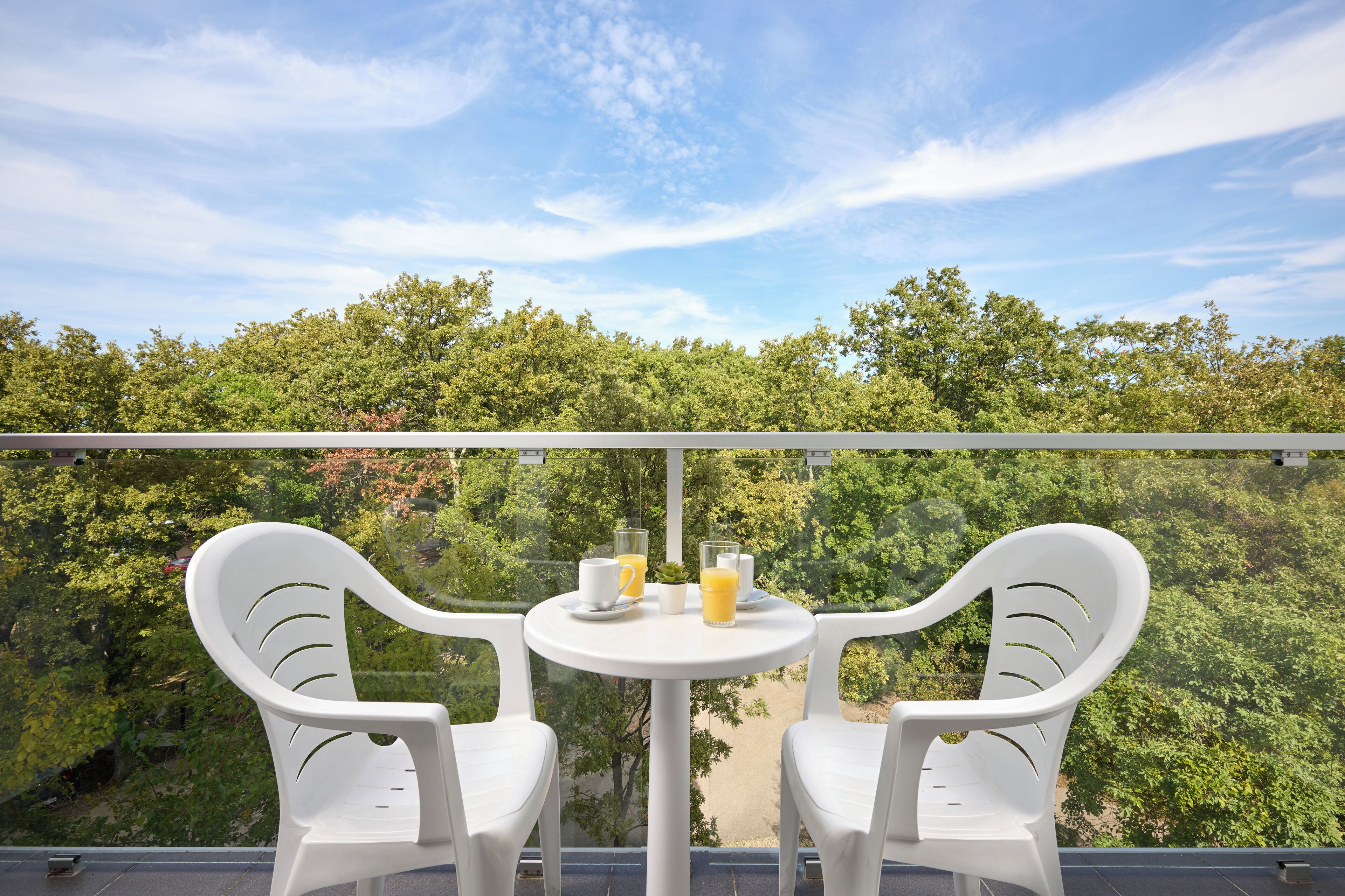 A balcony with two white plastic chairs and a small round table, with a glass of orange juice and a cup on it.