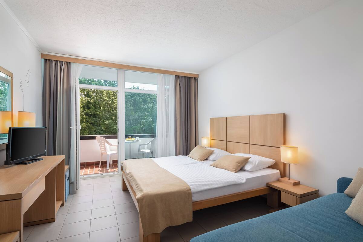 Ein Hotelzimmer mit Bett, Nachttisch, Fernseher und einem Balkon mit Stuhl.