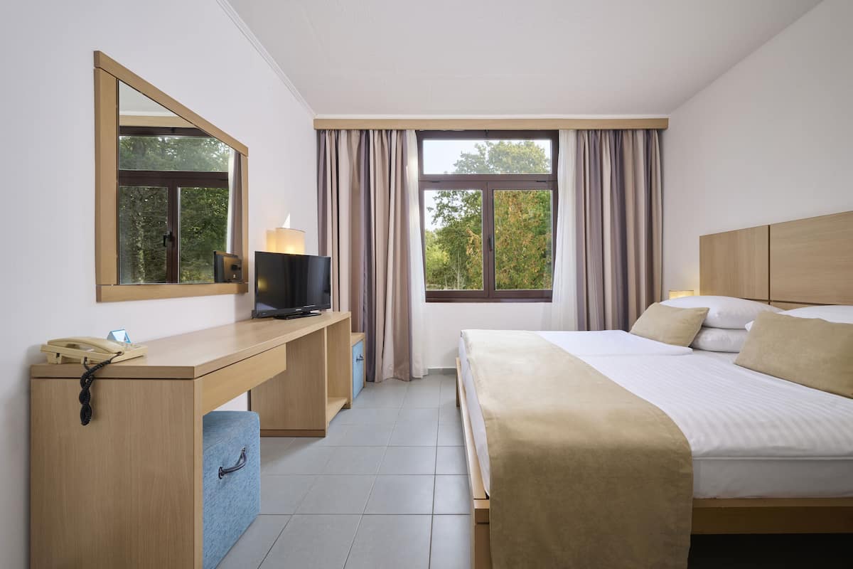Ein Hotelzimmer mit Bett, Schreibtisch mit Fernseher, Spiegel und einem Fenster mit Vorhängen.
