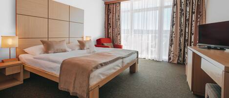 A hotel room with a large bed, a TV on a wooden cabinet, a red chair, and a large window with curtains.