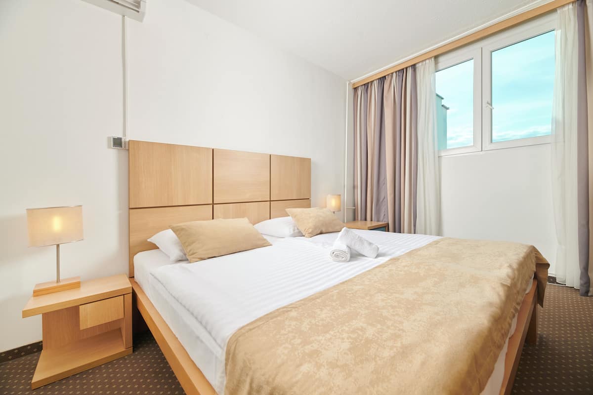Ein Hotelzimmer mit einem großen Bett, einem Holz-Kopfteil, einem Nachttisch mit Lampe und einem Fenster mit Vorhängen.