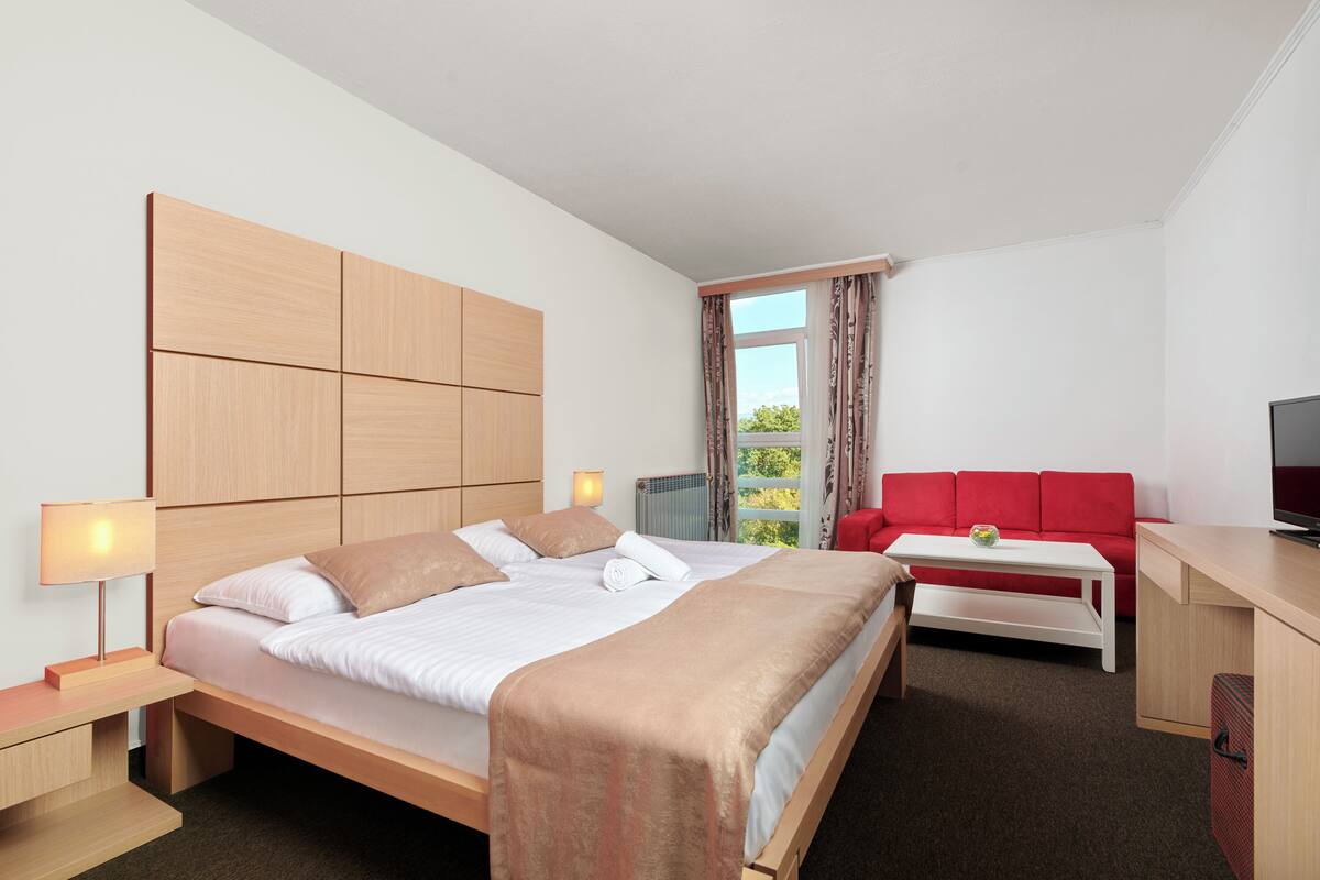 Ein Hotelzimmer mit Bett, Schreibtisch, einem roten Sofa und einem Fernseher.