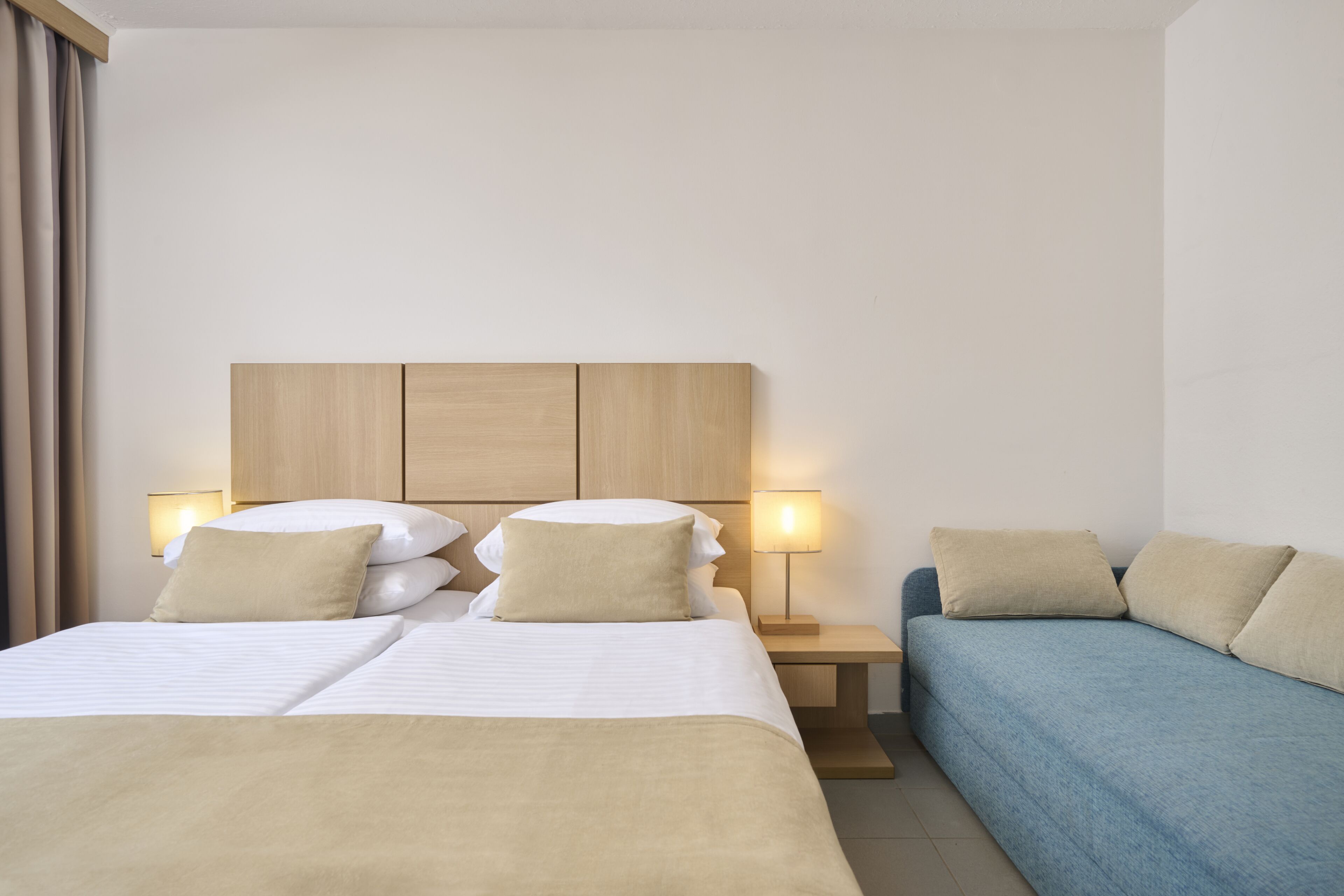 Hotellihuone, jossa on sänky, yöpöytä, lamppu ja sohva.