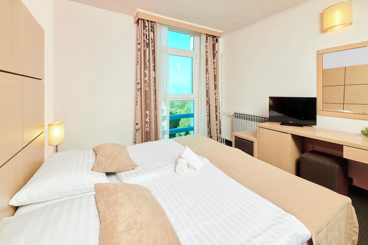 Ein Hotelzimmer mit zwei Betten, einem Schreibtisch mit Fernseher und einem Fenster mit Vorhängen.