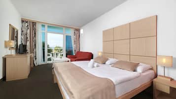 A hotel room with a large bed, a desk, a chair, a TV, and a window with curtains.