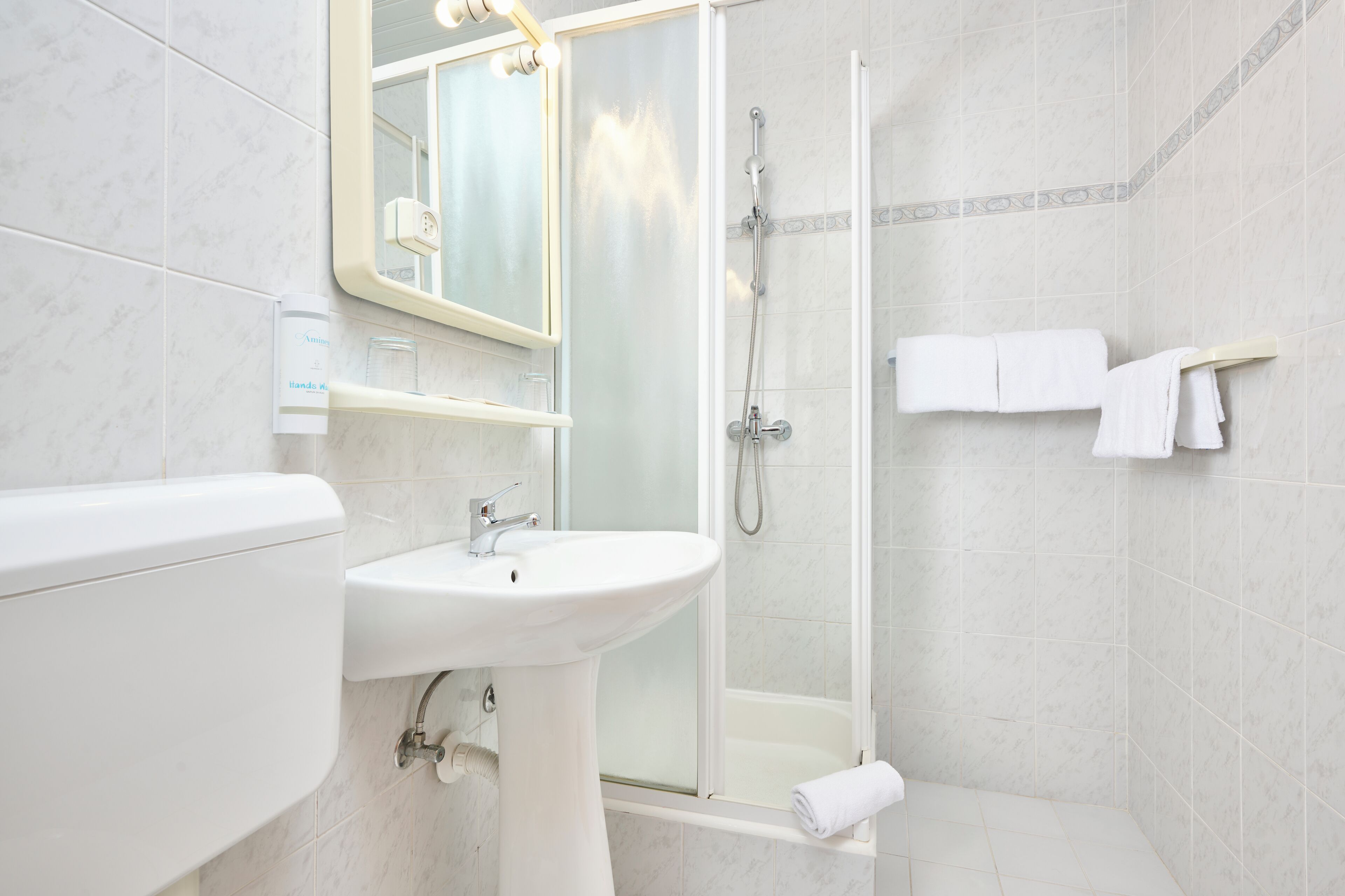A modern bathroom with a white sink, mirror, and glass-enclosed shower.