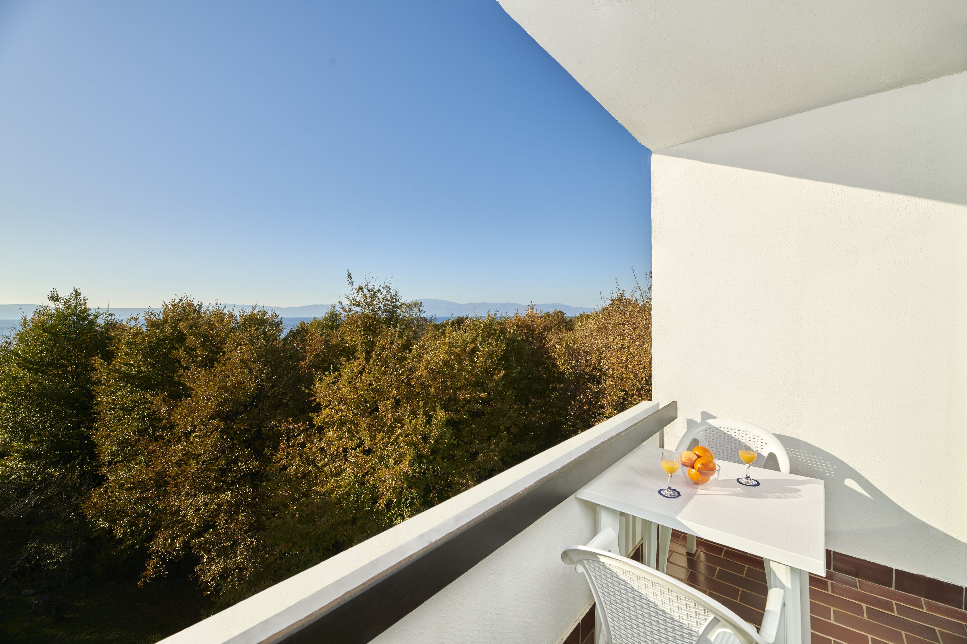 Un balcón con una mesa preparada para dos, con vistas a un área boscosa y una vista distante.