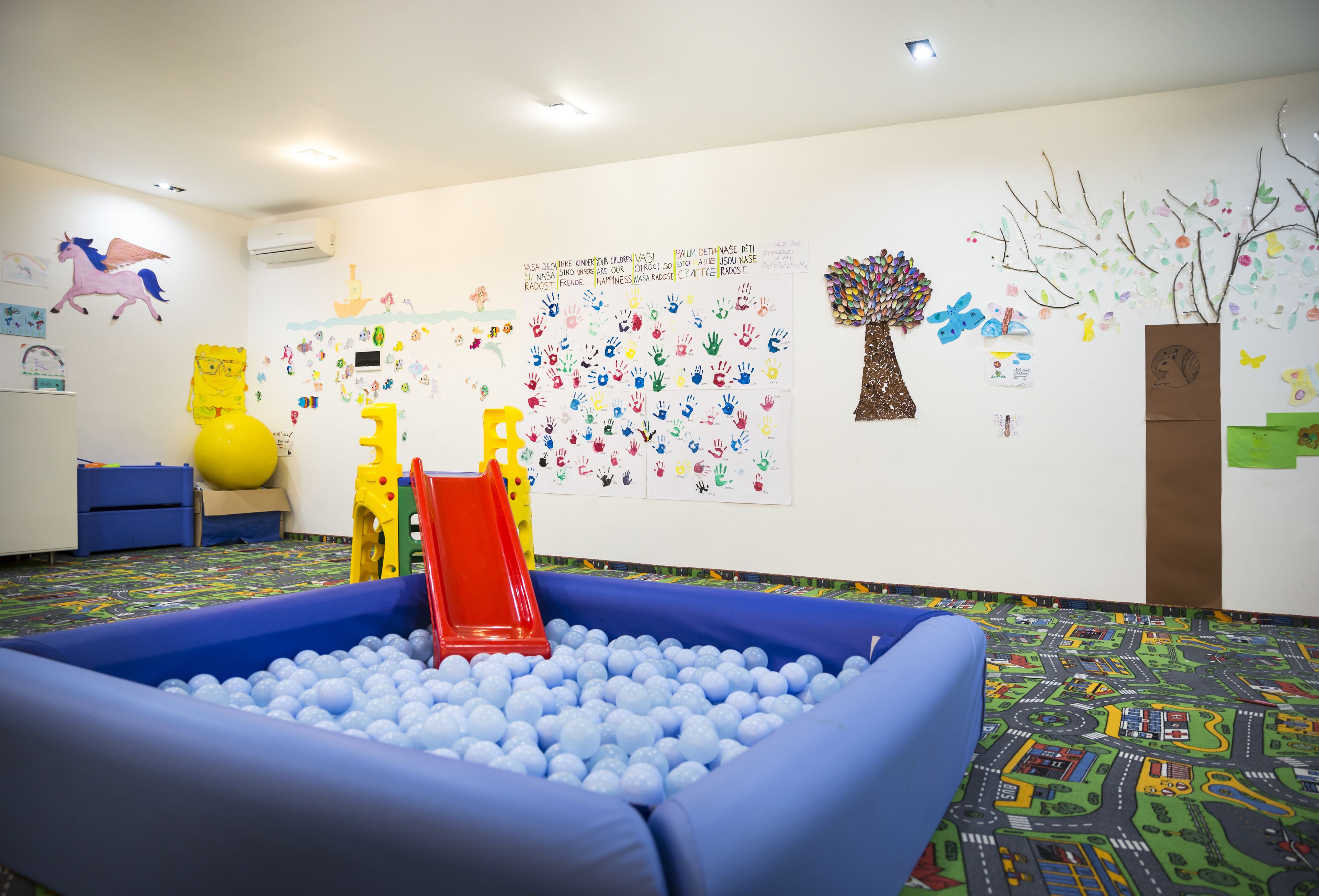 Ein Spielbereich für Kinder mit einem Ballbecken, bunten Wandbildern und einer Rutsche.