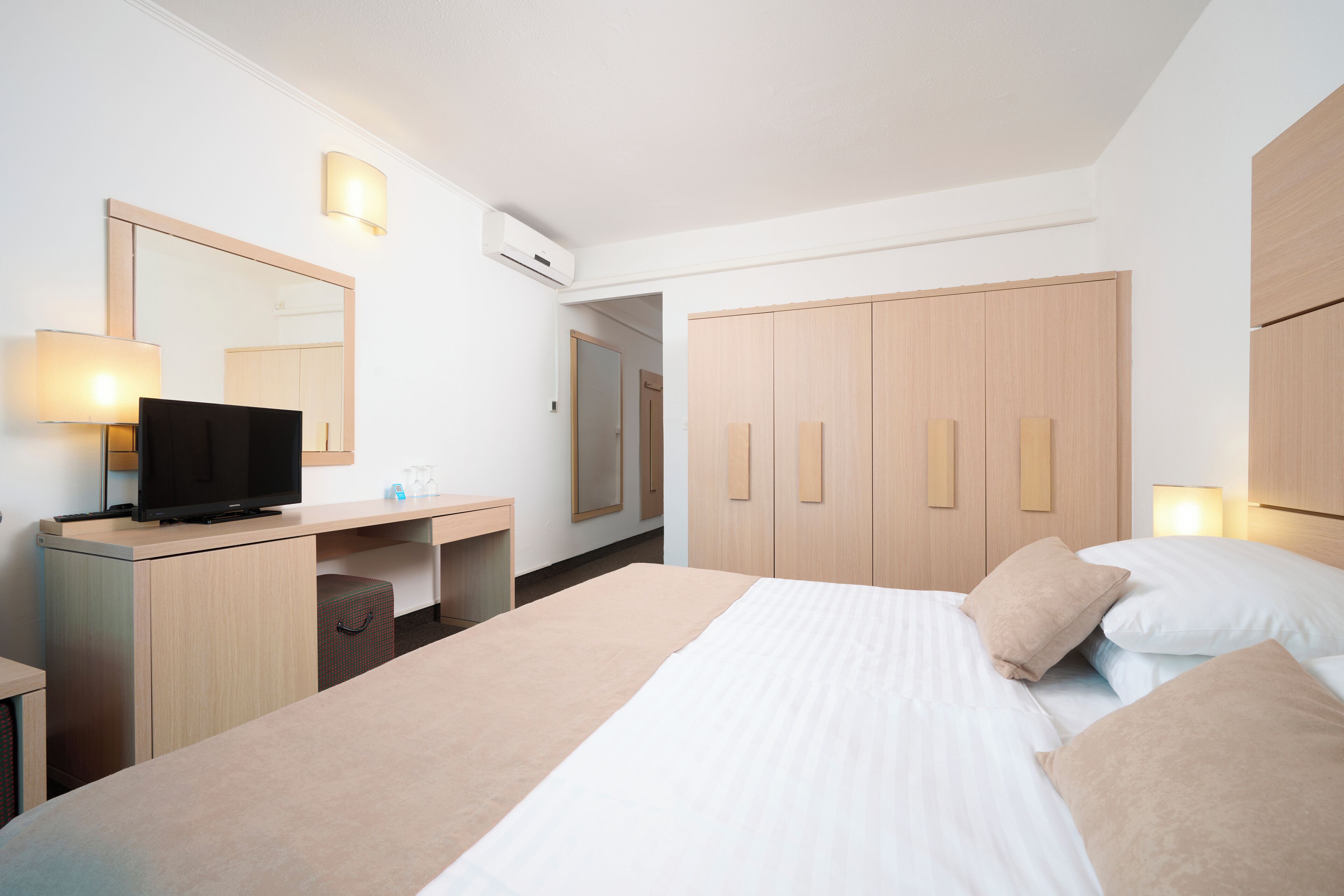 A hotel room with a bed, a desk, a television, and a wardrobe.