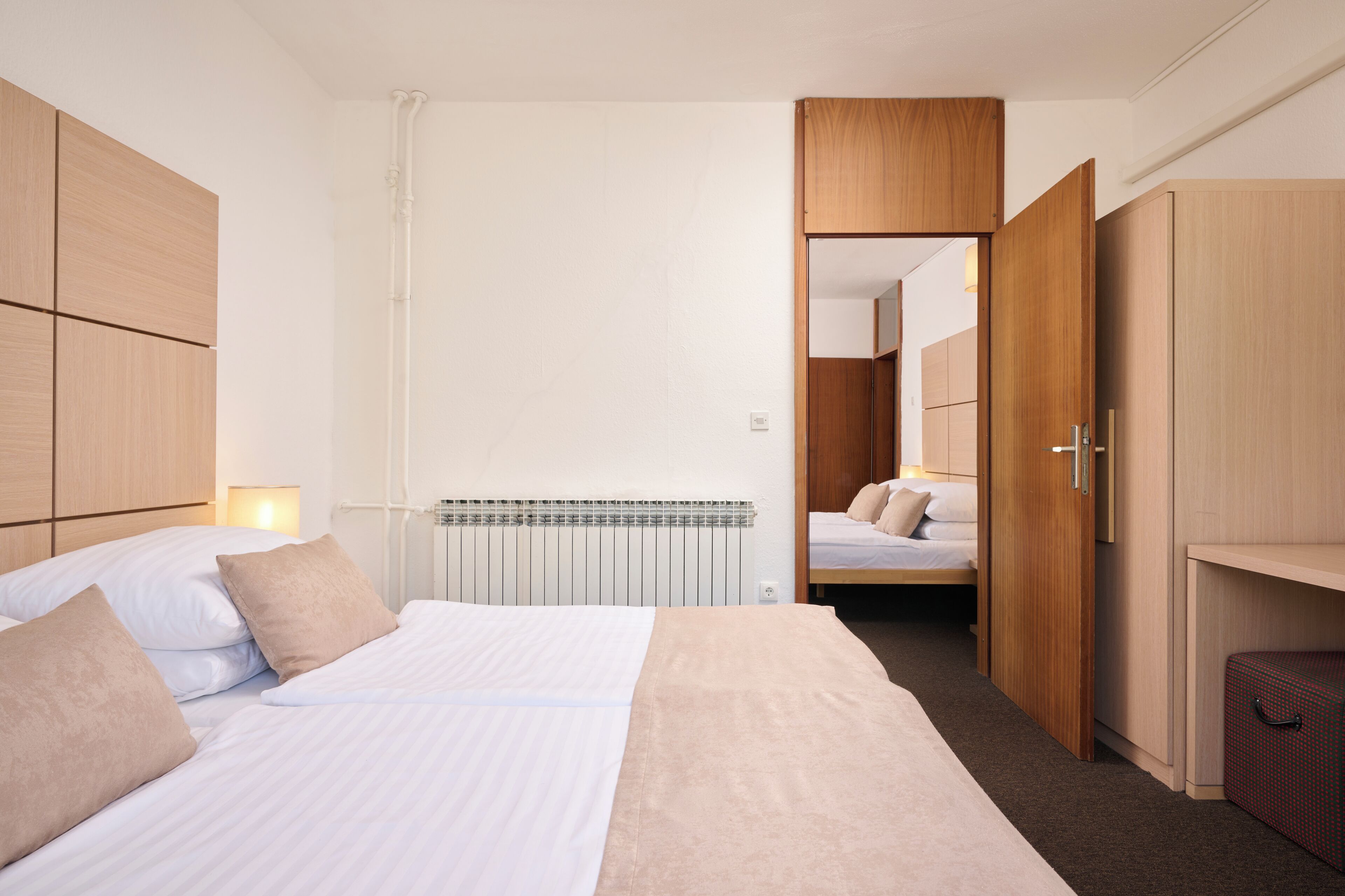 Une chambre d’hôtel avec un lit, une armoire en bois et une valise.