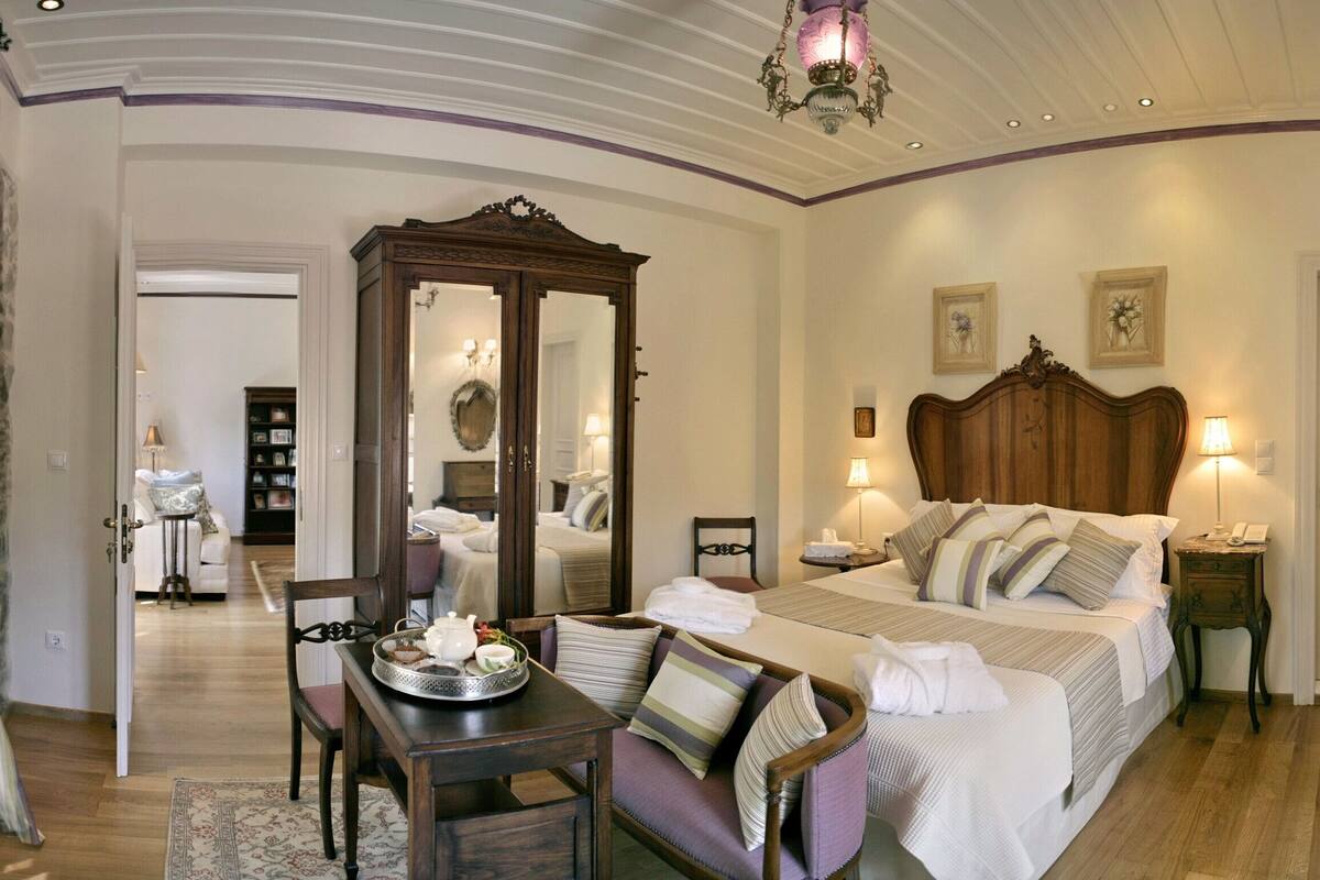 Une chambre d’hôtel avec un grand lit, un coin salon avec une table et des chaises, un miroir et une commode.