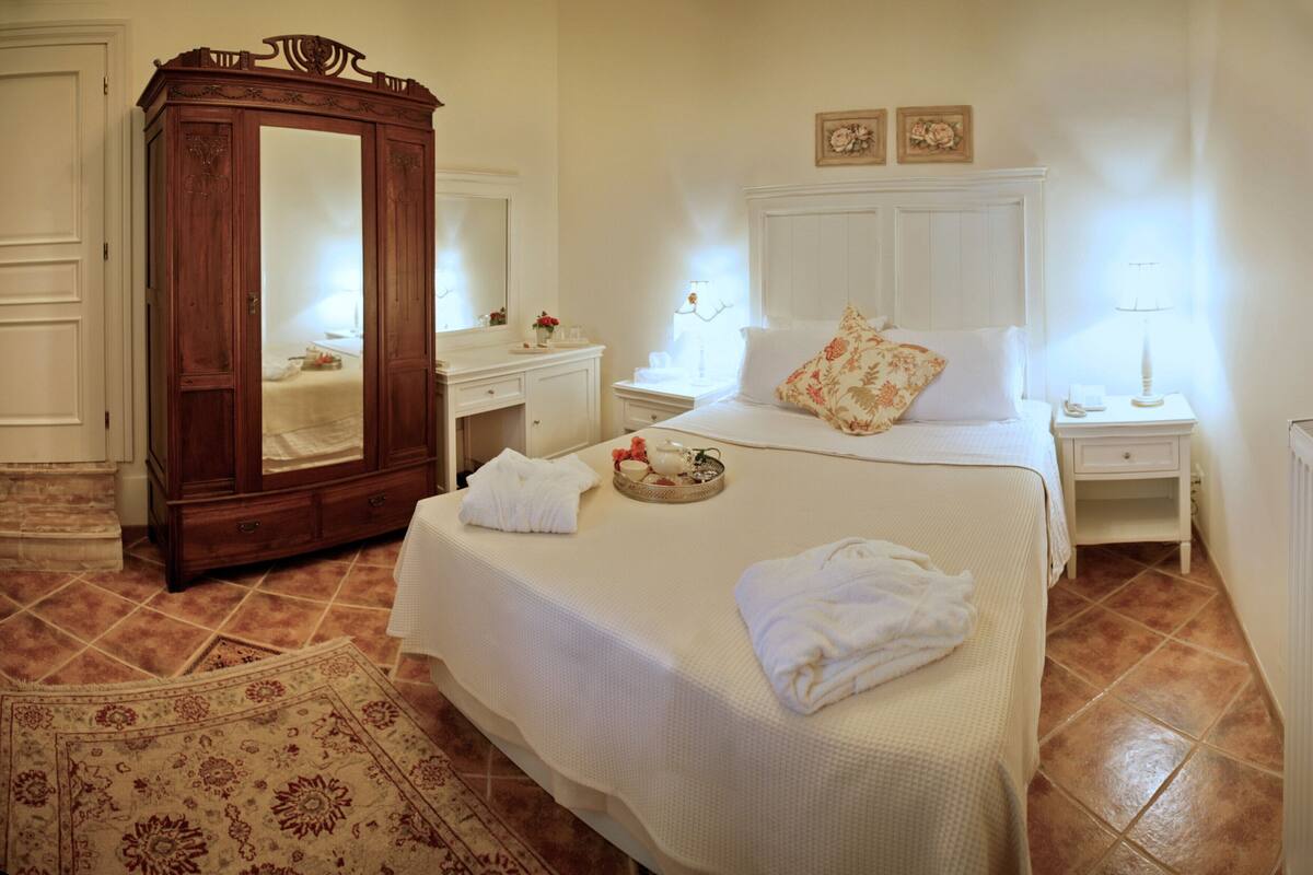 Une chambre d’hôtel avec un grand lit, une armoire en bois, une coiffeuse, un miroir, une table de chevet et un radiateur.