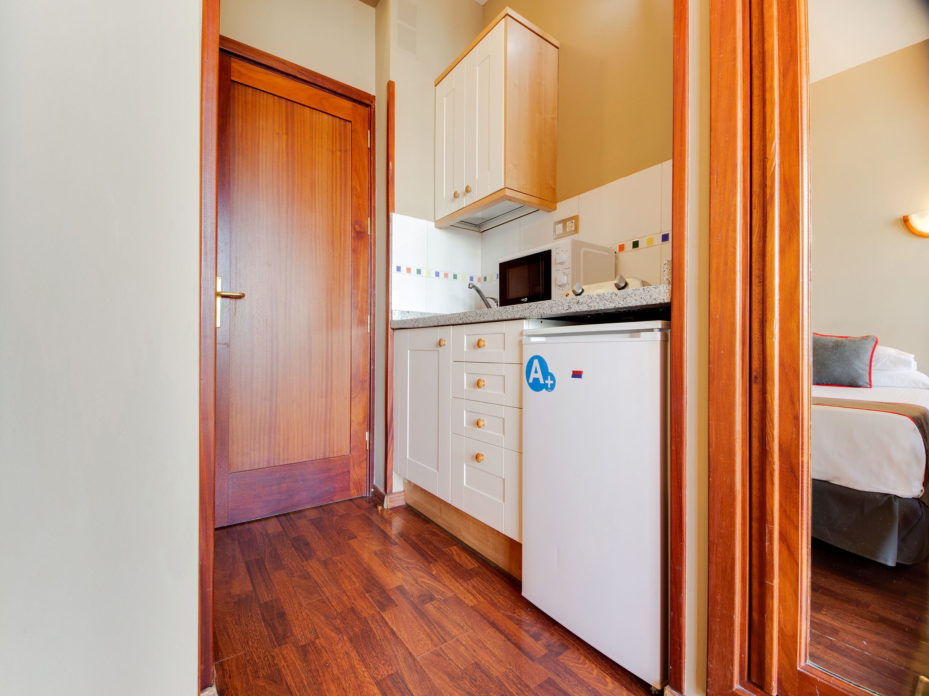 Een kleine keuken met houten kastjes, een magnetron en een koelkast.