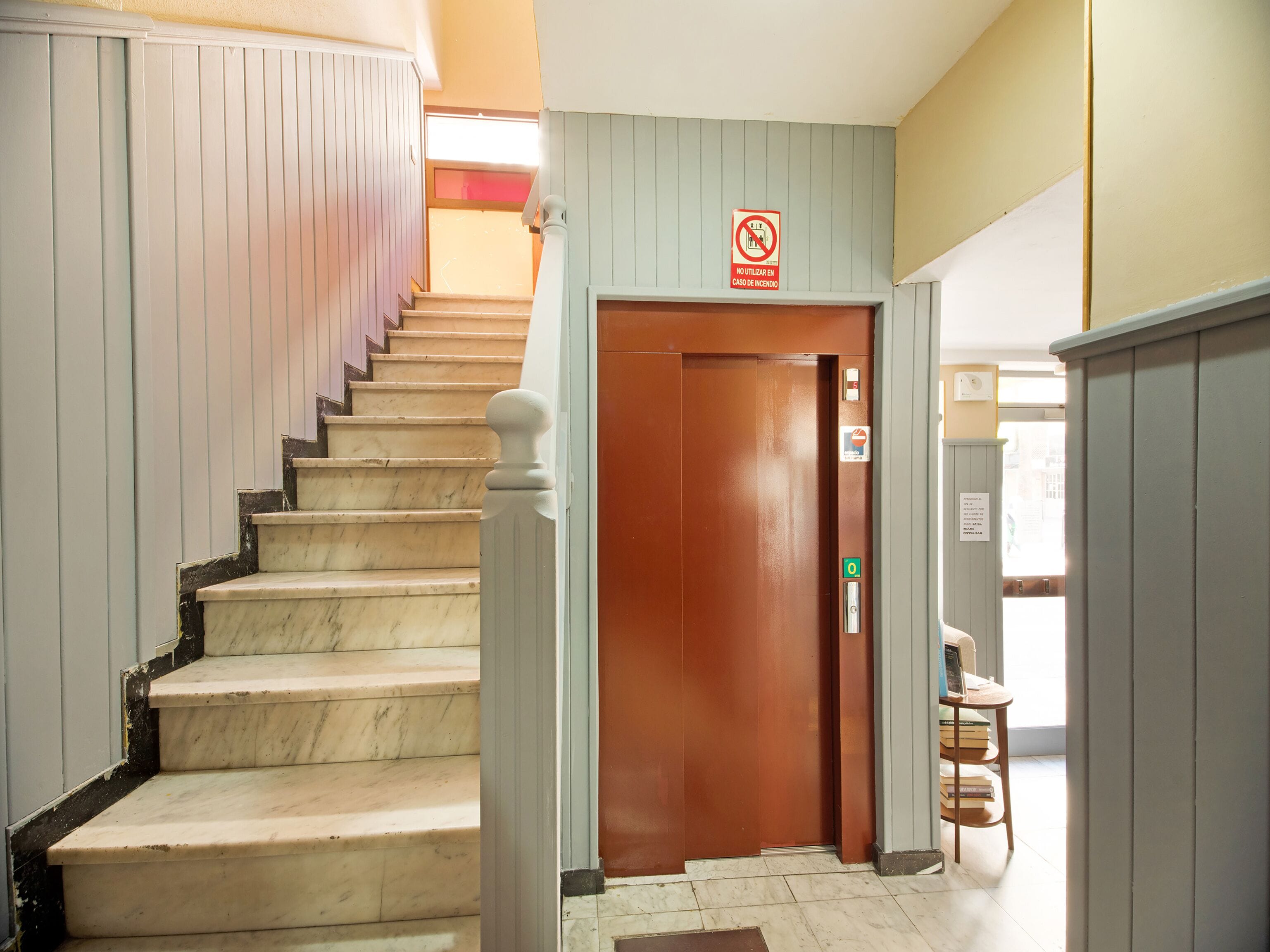 A staircase with a wooden door at the top, a no smoking sign, and a small table with books.