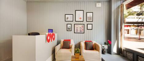 A reception area with a white reception desk, two sofas, a small table with a plant, and framed pictures on the wall.