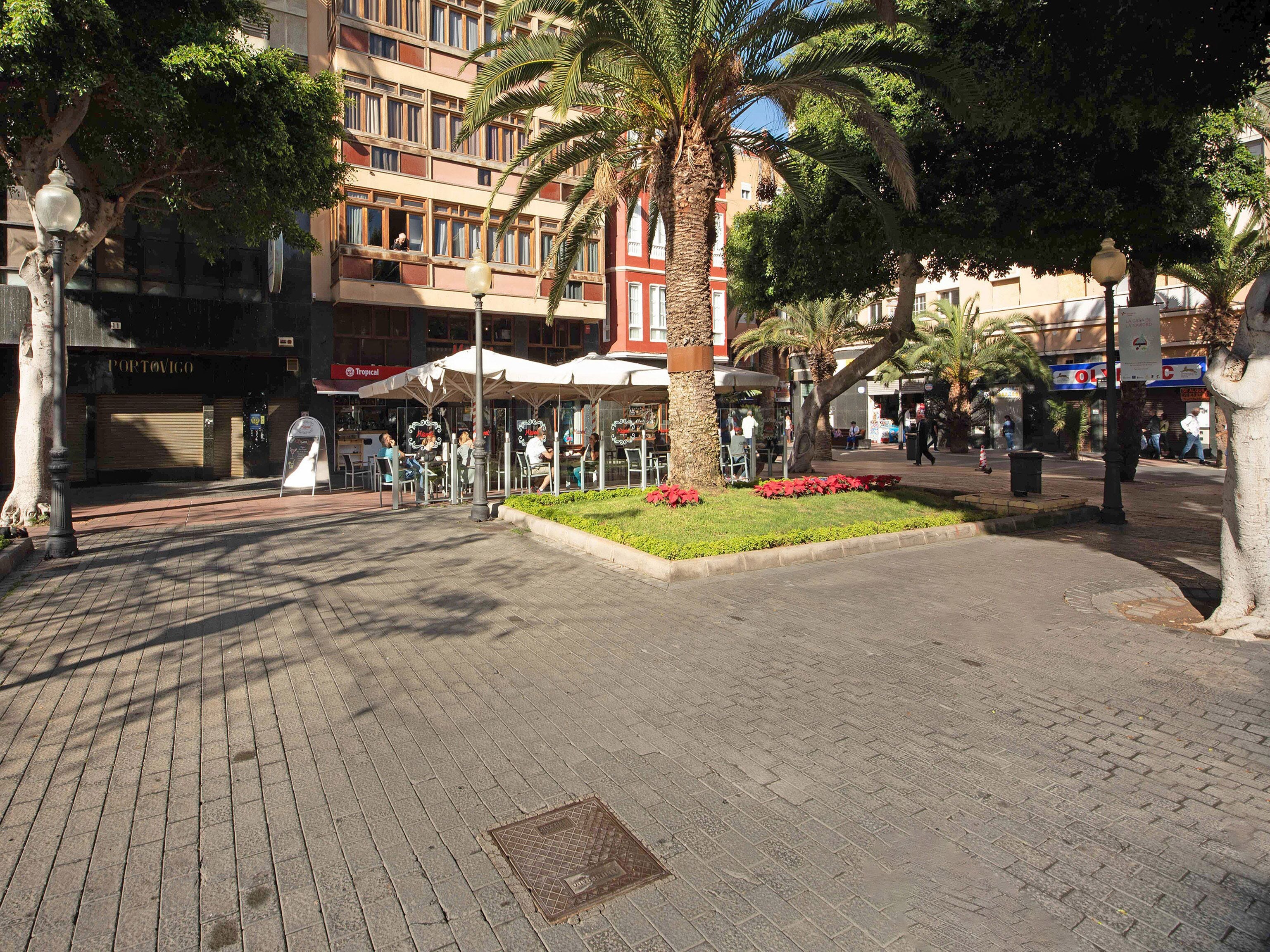 Uma praça pública com um jardim central, edifícios ao redor e áreas de estar ao ar livre.
