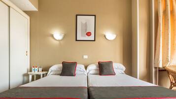 A hotel room with two beds, a framed picture on the wall, and two wall-mounted lamps.