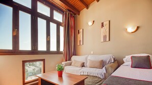 Een kamer met een groot raam, een bank, een bed, een kleine tafel en een potplant.