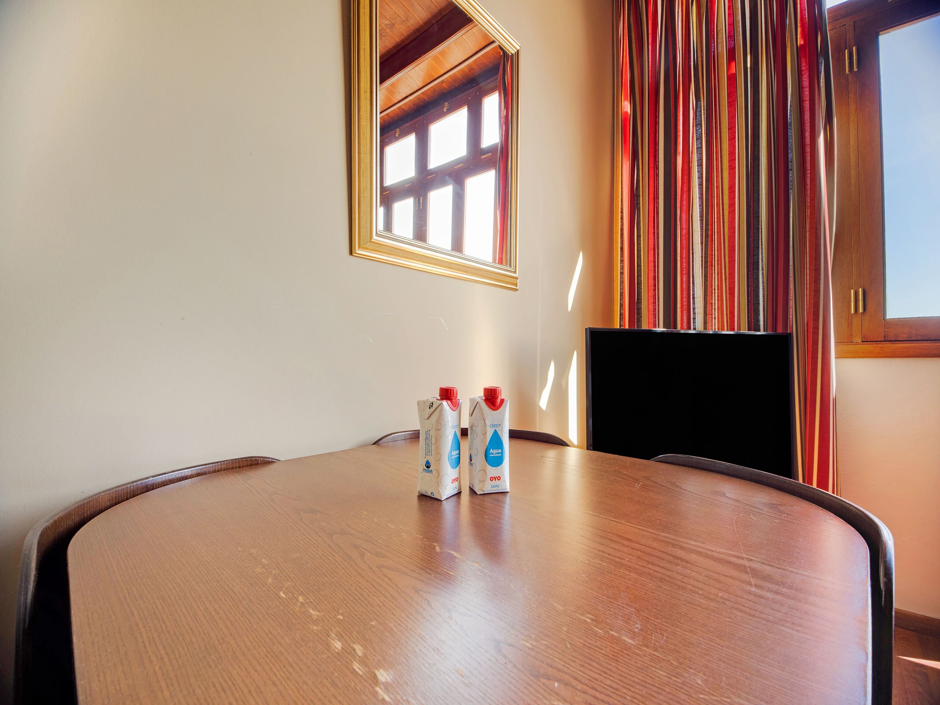 Un salón de conferencias con una mesa de madera, dos dispensadores de agua, un televisor y una ventana con cortinas a rayas.