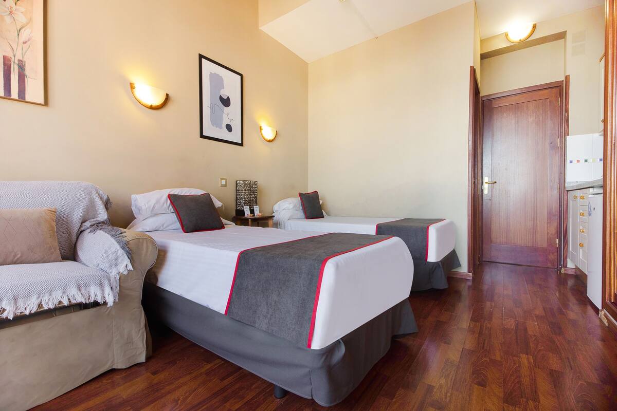A hotel room with two beds, a sofa, a small table, and a door leading to a bathroom.