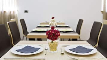 Une table à manger dressée pour deux personnes, avec des assiettes, des couverts et un vase rempli de fleurs rouges.