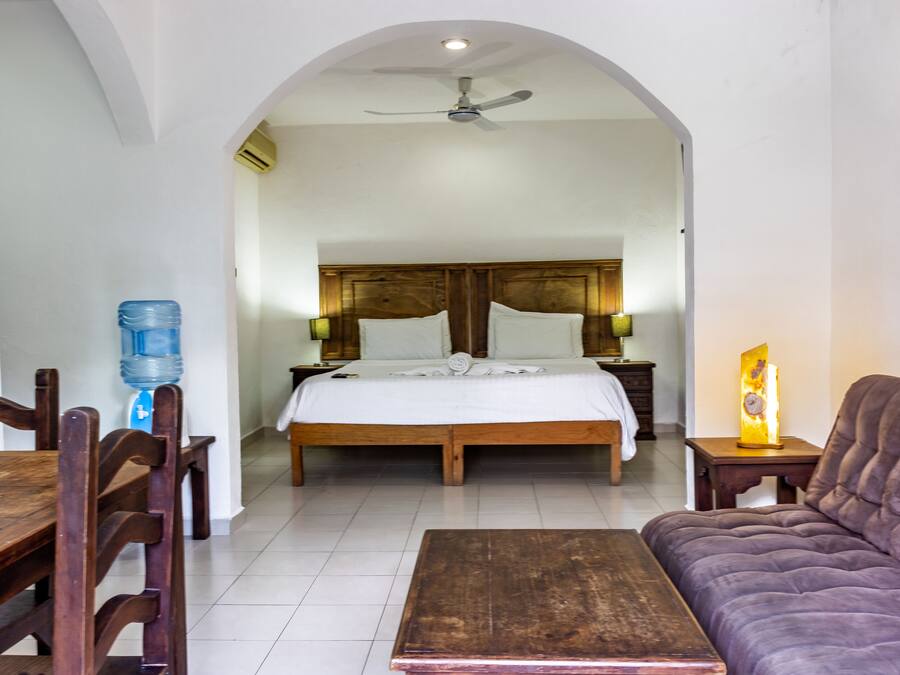 A bedroom with a large bed, wooden headboard, bedside tables with lamps, a wooden table, and a sofa.
