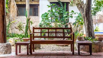 Un banco de madera con dos mesas a juego en un jardín con diversas plantas y un muro de piedra.
