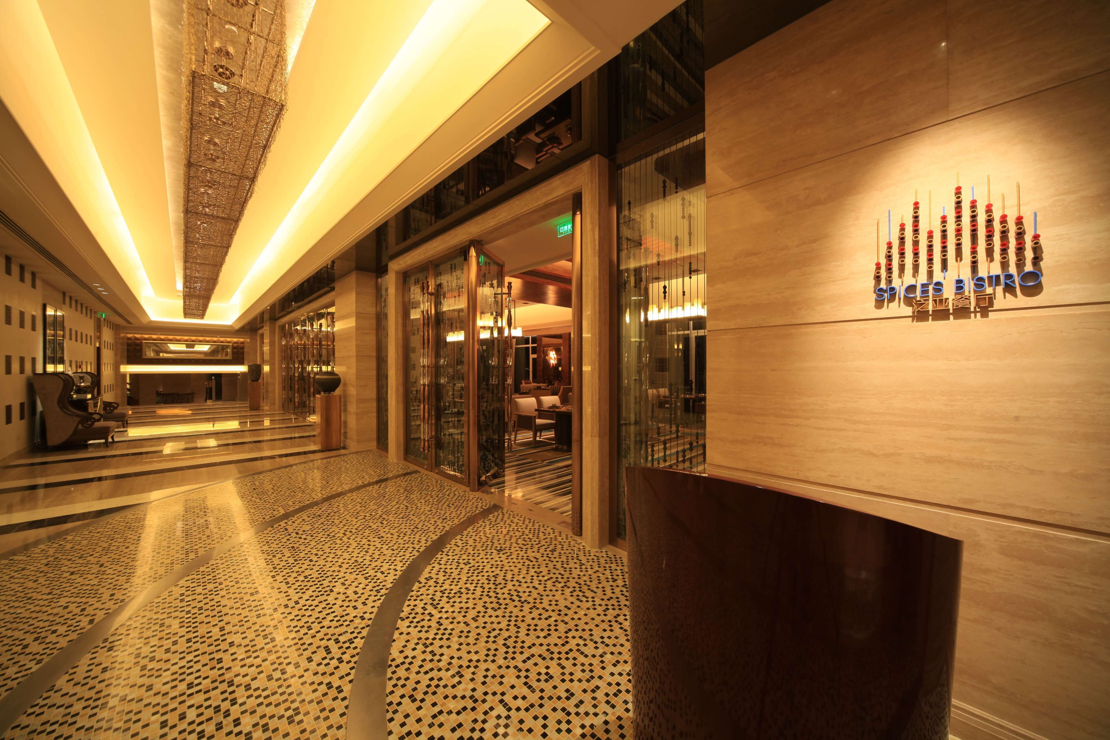 Un hall d’hôtel avec un sol à motifs, un comptoir d’accueil et une enseigne indiquant « Spices Bistro ».