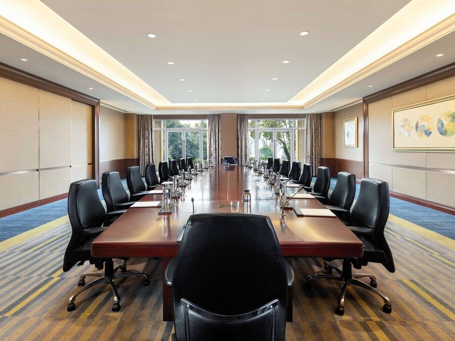 A conference room with a long table, multiple chairs, and a carpeted floor.