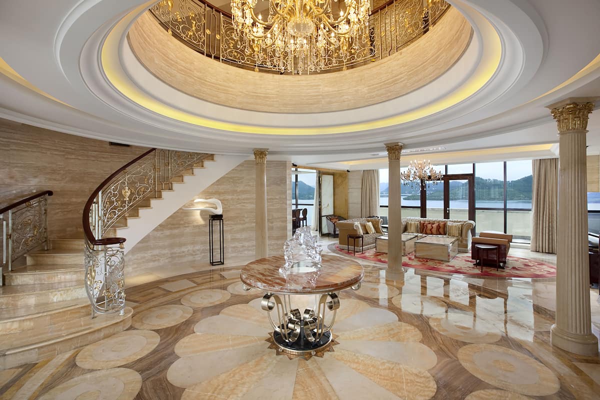 A luxurious interior with a grand staircase, a chandelier, and a seating area with a view of the outdoors.