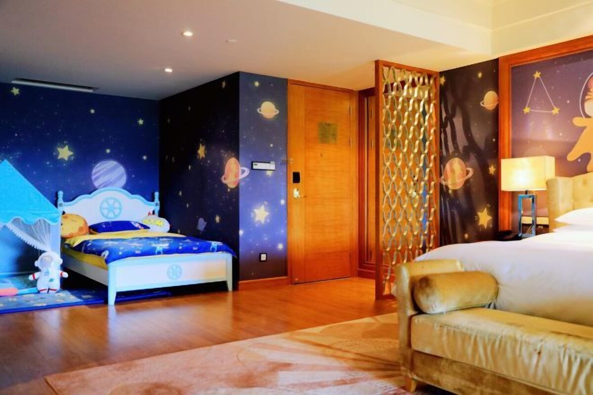 Un dormitorio con cama, mesita de noche, lámpara y pared con diseño de cielo estrellado.