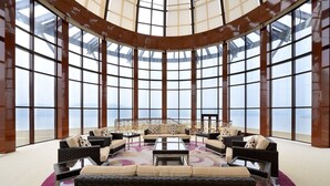 Un amplio salón con distribución circular, grandes ventanales y una zona de estar central con sofás y sillones.