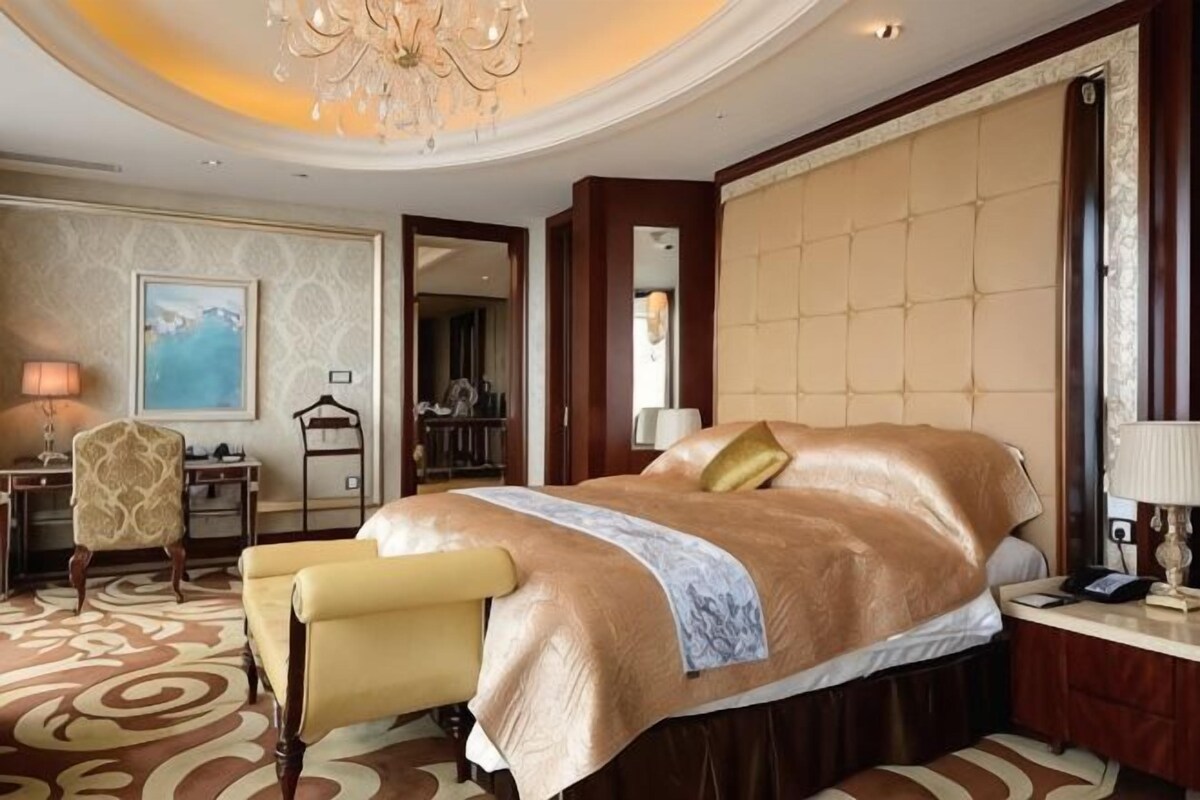 Una habitación de hotel con una cama grande, un escritorio, una silla, una araña y un cuadro en la pared.