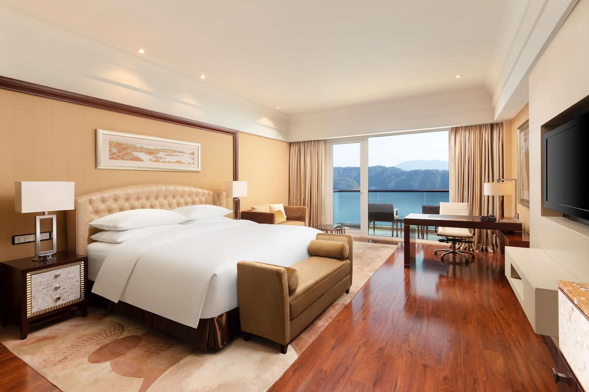 A spacious hotel room with a large bed, a desk, and a view of the mountains.