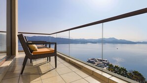 Un balcón con vistas a un lago tranquilo y montañas, una silla y una barandilla.