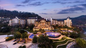 Un hotel grande con varias construcciones, un patio central con una piscina decorativa y zonas ajardinadas circundantes.