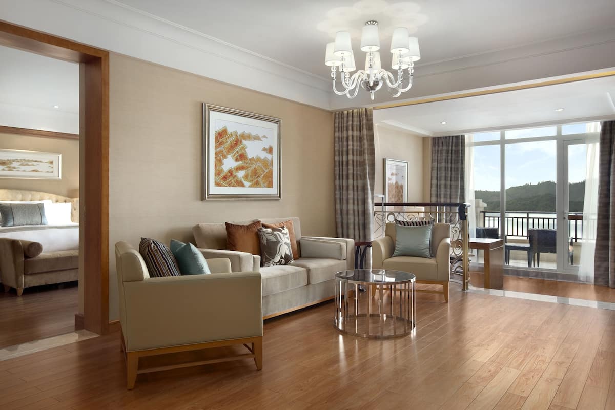 A spacious living room with a sofa, armchairs, and a coffee table. There is a large window with a view of the outdoors.
