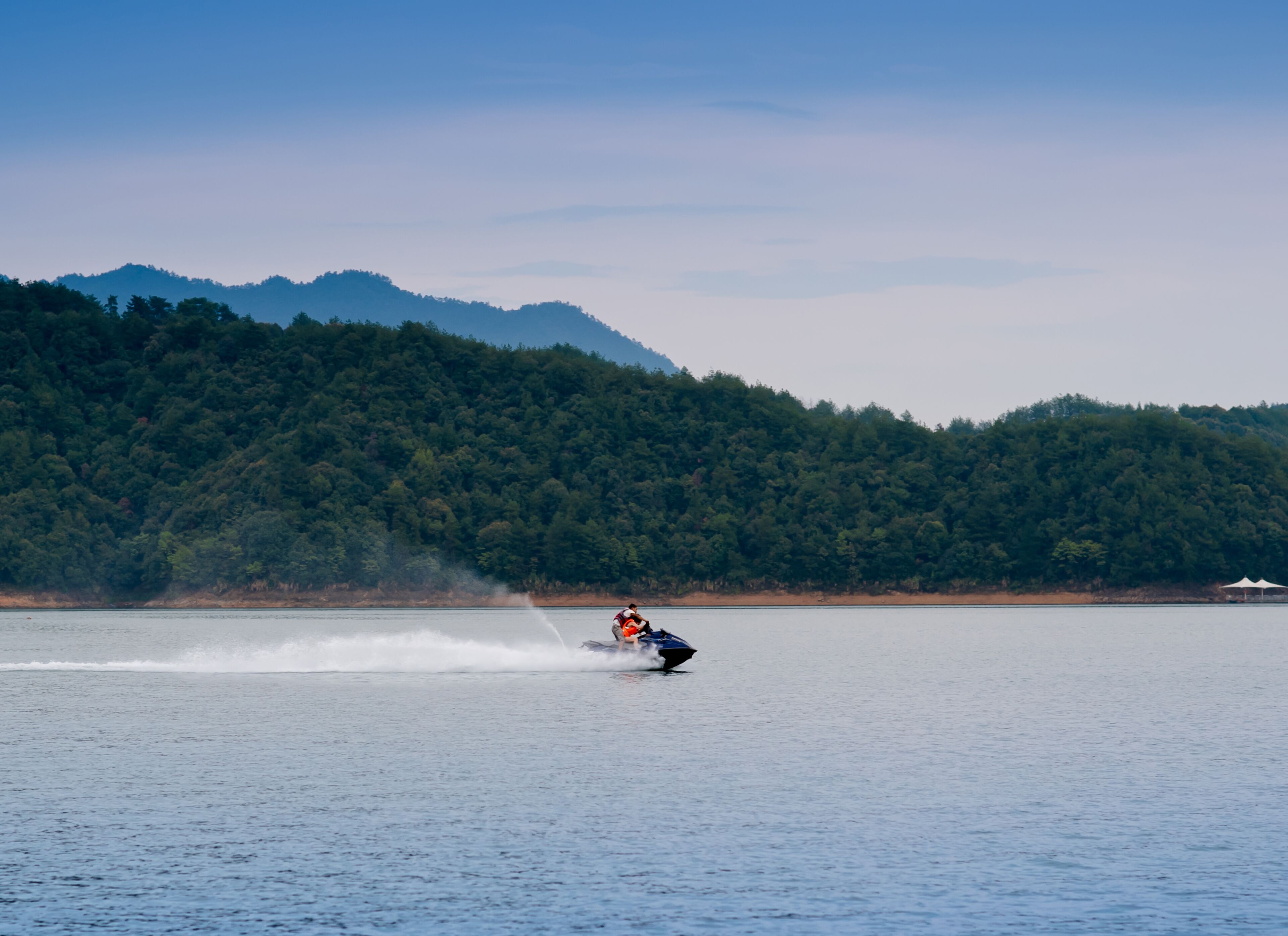 A person wakeboarding on a lake with a forested mountain in the background.