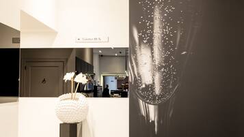 A modern interior with a reception desk, a white vase with flowers, and a large black and white photograph of a hand holding a glass.
