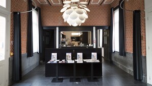 A reception area with a brick wall, a modern chandelier, and a reception desk with informational brochures. - Zimmerhof Hotel (Lier)