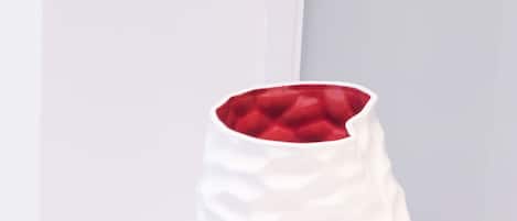 Un jarrón blanco con superficie texturizada y interior rojo, sobre una superficie blanca frente a una pared de color claro.