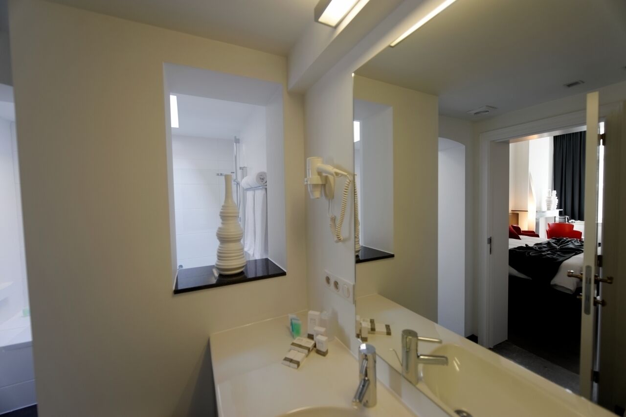 Bany d'hotel amb un mirall gran, un lavabo, un assecador i un telèfon.