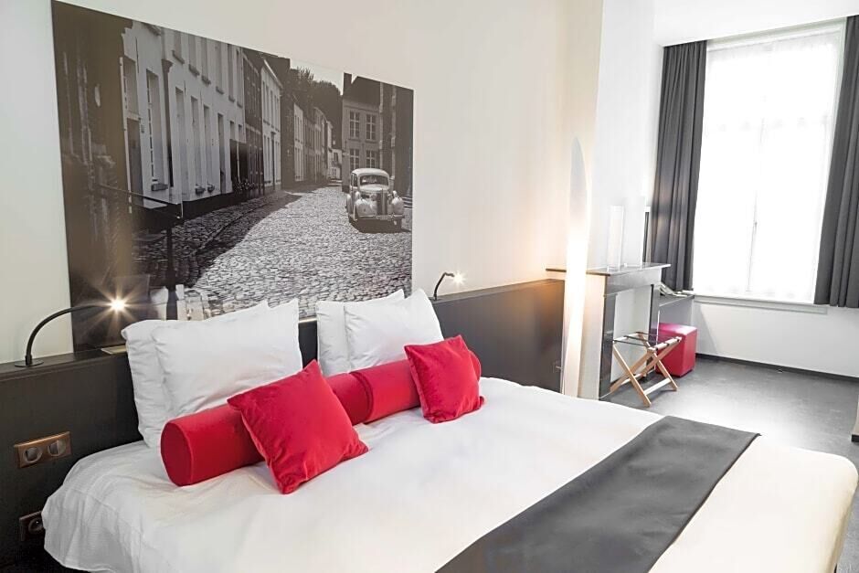 A hotel room with a large bed, a nightstand, a desk, and a window with curtains.