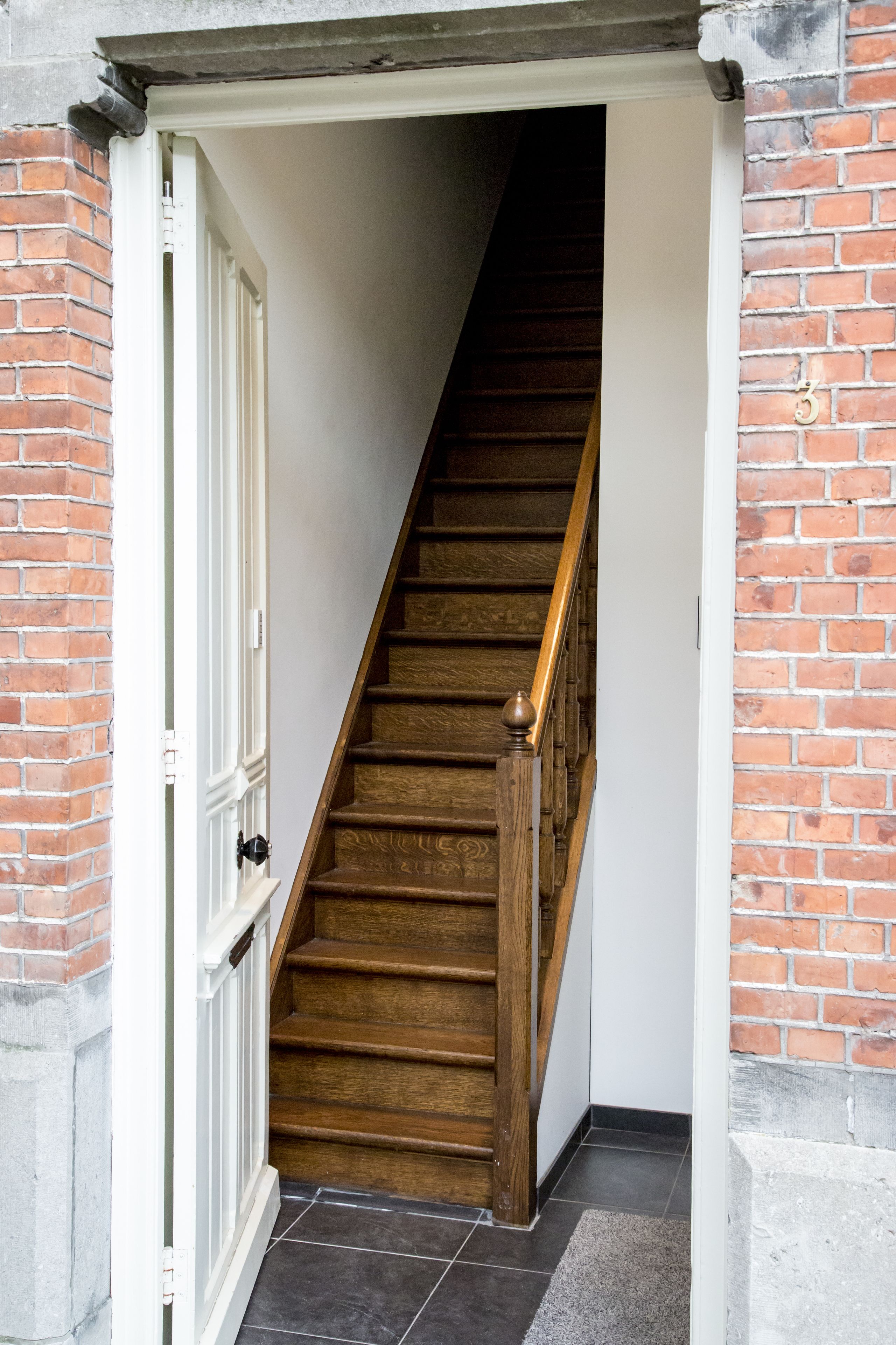 Een trap met houten treden en een leuning, die leidt naar een binnenruimte.
