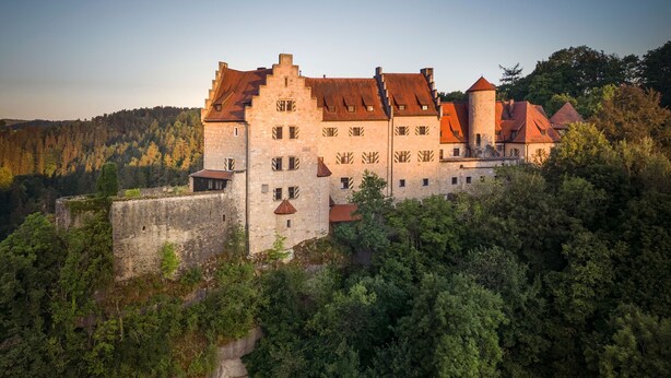 A historic castle with multiple towers and a fortified wall, surrounded by dense forest. - Burg Rabenstein (Ahorntal)