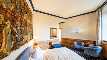Ein Hotelzimmer mit einem großen Bett, einem blau gestreiften Sessel, einem kleinen Tisch, einem Spiegel und einem Wandteppich zur Dekoration.