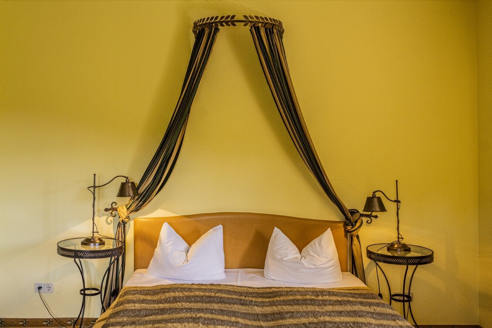 A bed with a canopy, two bedside tables with lamps, and a striped blanket.