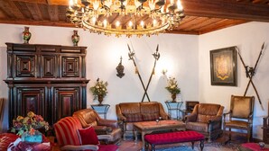 A traditional room with a wooden ceiling, a large chandelier, leather armchairs, a wooden cabinet, and a framed coat of arms on the wall. - Burg Rabenstein (Ahorntal)