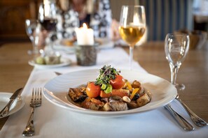 A dining table with a plate of food, a candle, and a glass of wine.